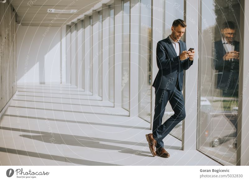 Junger Geschäftsmann, der ein Mobiltelefon in einem modernen Büroflur benutzt Smartphone Gebäude Raum professionell Exekutive Mitteilung benutzend Flur Telefon
