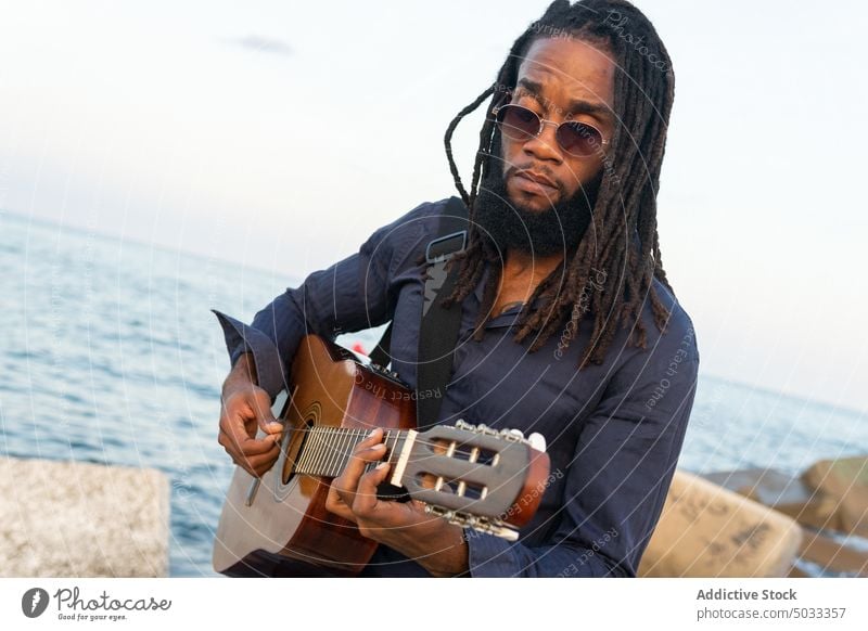 Afroamerikanischer Musiker spielt Gitarre an der Küste in der Nähe der Stadt Mann Gitarrenspieler spielen Kälte Fluss Stauanlage ausführen akustisch männlich