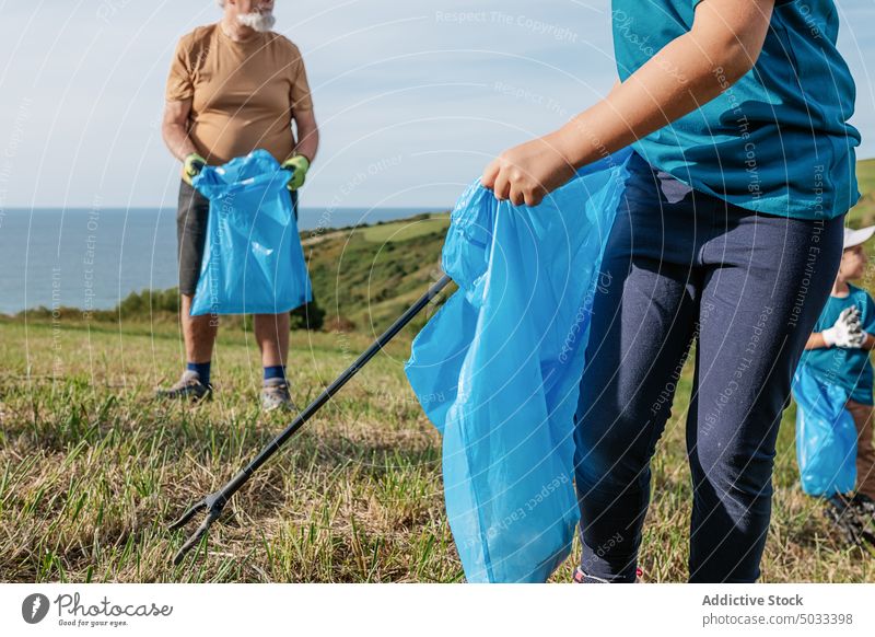 Erntehelferin und älterer Mann sammeln Müll auf einem Feld Mädchen Kind Junge Großvater Rentnerin abholen Tasche Müllzange Natur MEER grün Freiwilliger Sommer