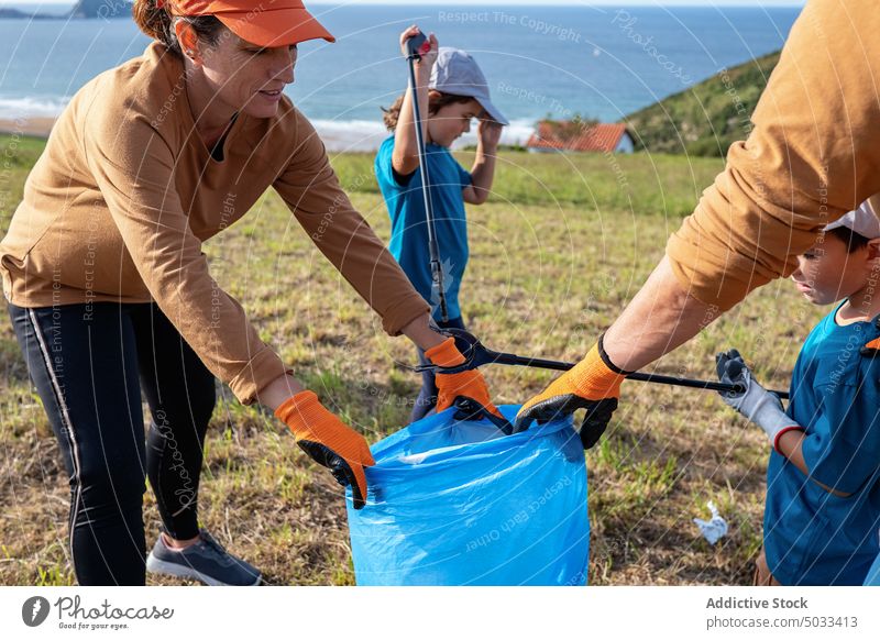 Familie mit Kindern sammelt gemeinsam Müll auf einem Feld Freiwilliger abholen Ökologie Umwelt pflücken Drückerzange umweltfreundlich Hügel MEER wiederverwerten