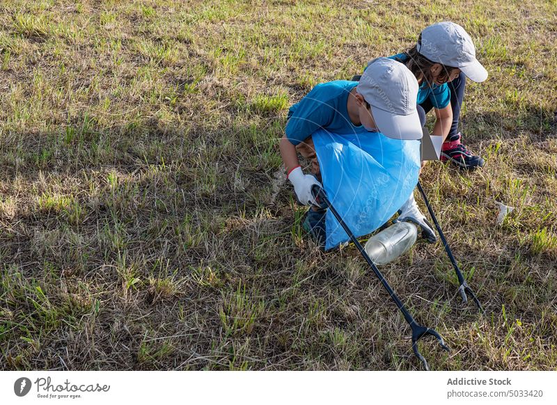 Kinder mit Müllzangen beim Müllsammeln Freiwilliger abholen Abfall Kunststoff Rasen Gras Umwelt Ökologie umweltfreundlich Tasche verschmutzen Sommer Natur