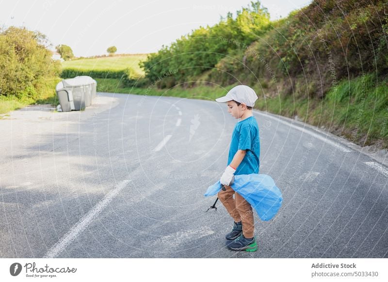 Junge mit Müllsack läuft über die Straße Kind Spaziergang Asphalt Tasche Handschuh Freiwilliger Behälter Müllzange Ökologie wiederverwerten Abfall Pflege
