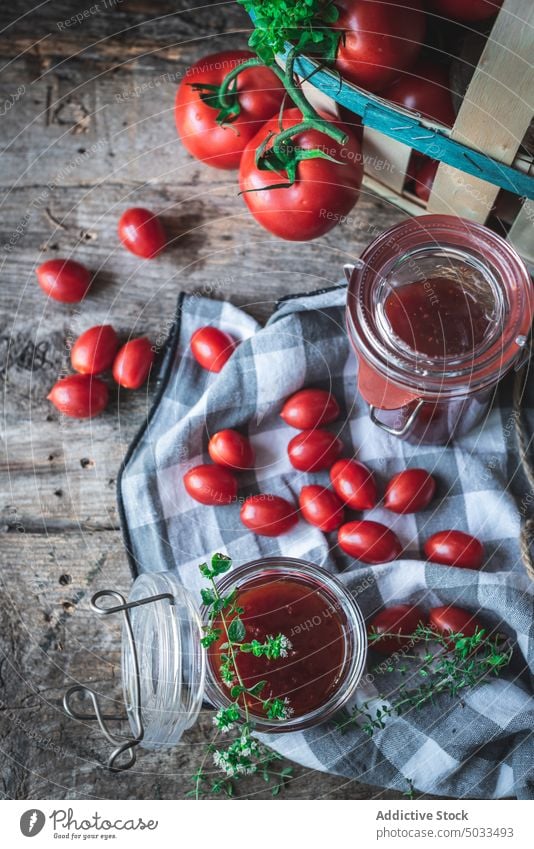 Tomaten und Kräuter neben Gläsern mit Marmelade Kraut Tisch Korb Serviette rustikal frisch Glas Zusammensetzung Küche reif Lebensmittel organisch Bestandteil