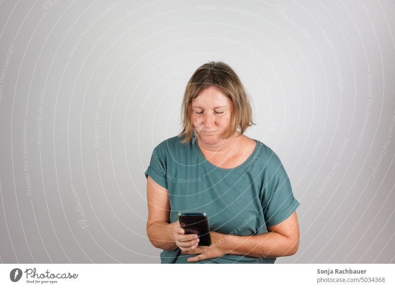 Eine Frau mit Bauchschmerzen hält ein Smartphone in der Hand. Notruf. frau smartphone bauchschmerzen Innenaufnahme gesundheit 50 plus Krampf Verzweiflung Hilfe