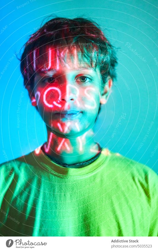 Ernster Junge mit Neonaufschrift im Gesicht Kind Porträt ernst emotionslos leuchten neonfarbig Licht Aufschrift Brief orange nachdenklich Kindheit Windstille
