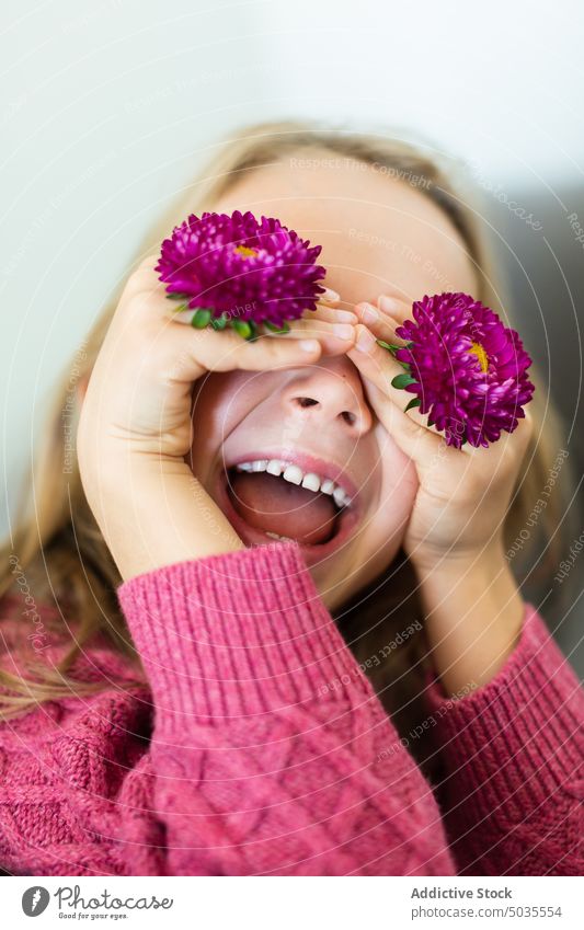 Mädchen bedeckt Augen mit blühenden Blumen Porträt Lächeln Kind Augen abdecken positiv Blütezeit Pullover purpur blond Glück heiter froh Freude schüchtern warm