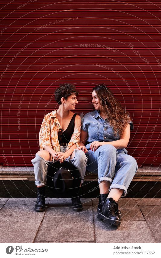 Lesbisches Paar sitzt in der Nähe der roten Wand Frauen Lächeln Termin & Datum Freundin Borte Glück Gebäude Straße Madrid Spanien jung Zusammensein Freundschaft
