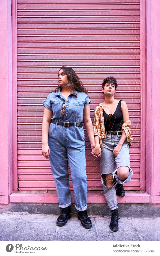 Lesbisches Paar lehnt sich an rosa Wand Frauen Straße fettarm Händchenhalten Zusammensein Stil Freundin Partnerschaft Madrid Spanien jung romantisch lgbt