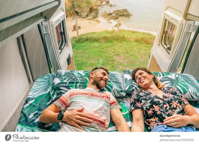 Pärchen, das sich auf dem Bett seines Wohnmobils anschaut Glück Paar die sich gegenseitig ansehen Lügen Landschaft Ausflug Küste offen Tür Liebe Fröhlichkeit
