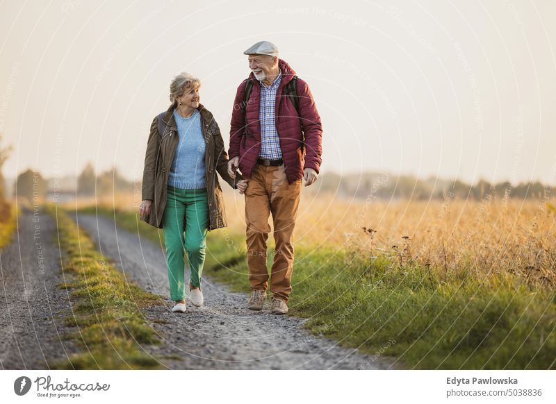 Älteres Paar auf einem Feld im Herbst bei Sonnenuntergang laufen Ausflug Rucksack Seniorenpaar Frau Zwei Personen Mann reif Zusammensein alt Menschen