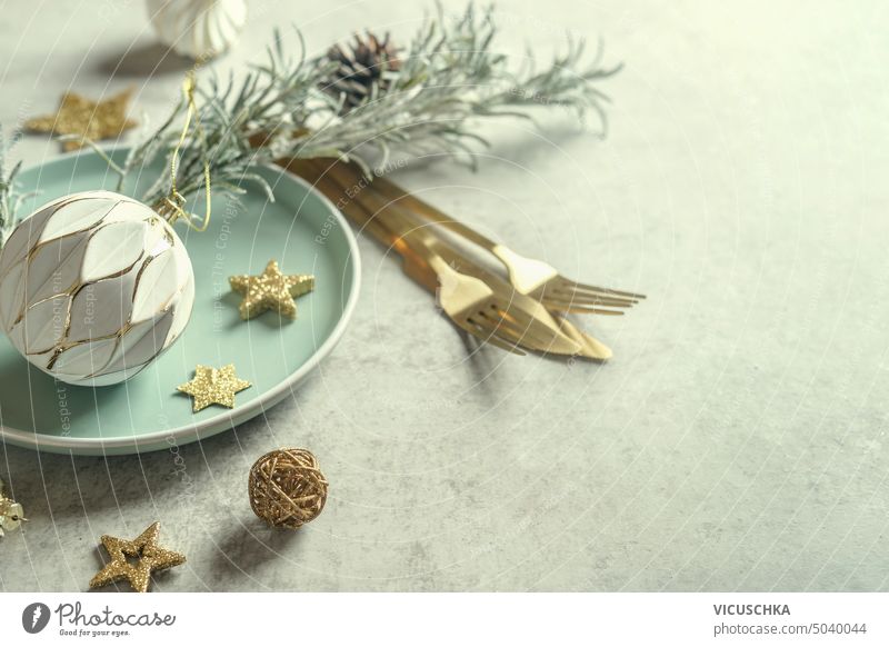 Weihnachtliche Tischdekoration für das Weihnachtsessen mit Teller, goldenem Besteck und Dekoration aus alten Kugeln, Sternen und Tannenzweigen Feiertag
