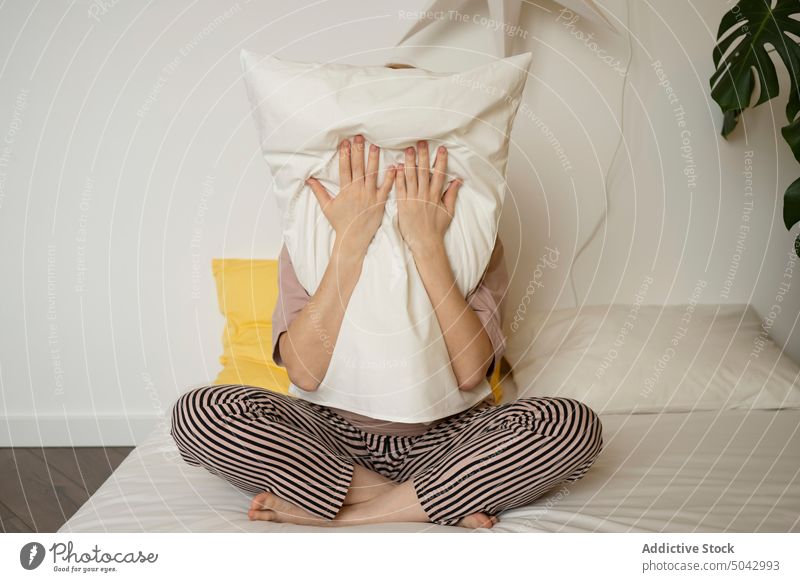 Anonyme Frau auf Bett sitzend mit Kopfkissen Schlafzimmer Umarmung Tierhaut Komfort Pyjama heimwärts Morgen Umarmen weich Beine gekreuzt Nachtwäsche Dame