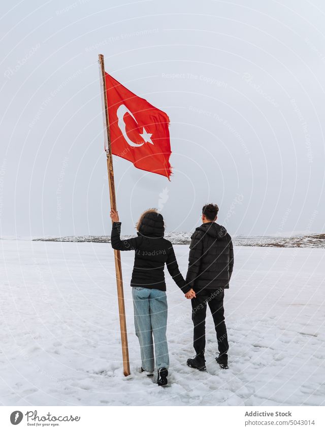 Unbekanntes reisendes Paar mit türkischer Flagge, das sich auf verschneitem Gelände an den Händen hält Händchenhalten Fahne Partnerschaft Ausflug Tourist