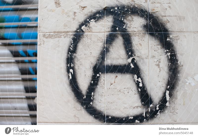 Graffiti an der Wand mit einem schwarzen Anarchie-Symbol Zeichen auf einer grauen Wand. Grunge-Tapete Hintergrund. Anarchistische politische Graffiti