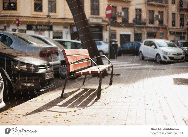 Eine Holzbank in der Stadt mit geparkten Autos auf der Straße an einem sonnigen Morgen sich[Akk] entspannen Herbst Bank Großstadt farbenfroh ruhen urban fallen