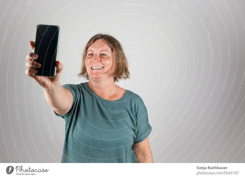 Eine Frau über 50 macht mit einem Smartphone ein Selfie selfie Lifestyle Lächeln heiter Studioaufnahme 50 plus Fröhlichkeit Glück Spaß Technik & Technologie