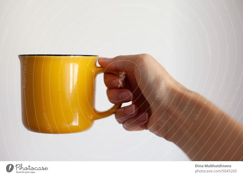 Frau hält gelbe Tasse auf weißem Hintergrund Nahaufnahme. Gelber Becher mock up für das Einfügen Design.  Trinken von Kaffee oder Tee am Morgen oder während der Pause von der Arbeit.