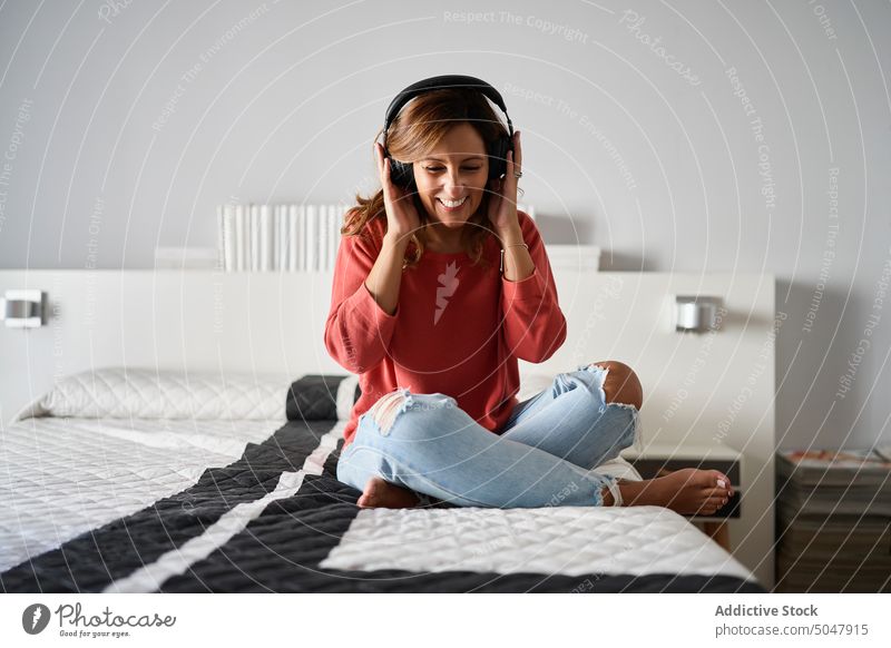 Frau beim Musikhören auf dem Bett zuhören heimwärts Wochenende Schlafzimmer Kopfhörer berühren meloman hispanisch ethnisch Lebensmitte reif lässig