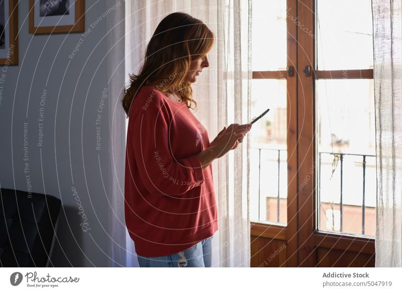 Reife Frau sendet eine Textnachricht Lächeln Nachricht Smartphone Fenster benutzend Browsen senden Glück heimwärts Lebensmitte reif hispanisch ethnisch Internet