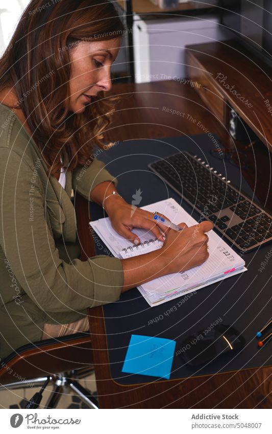Konzentrierte Frau schreibt in Notizblock im Büro zur Kenntnis nehmen schreiben freiberuflich Computer Arbeit selbständig unabhängig Notebook Tisch Zeitvertreib