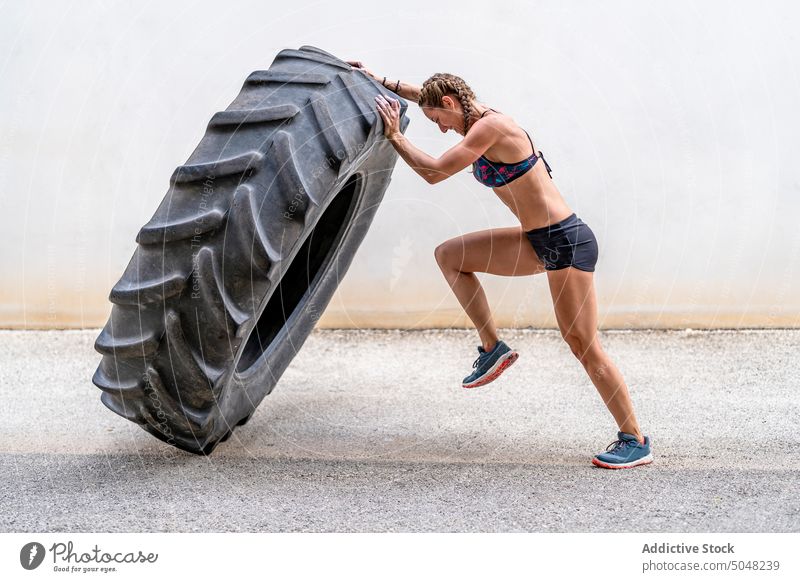 Weibliche Athletin hebt schweren Reifen Sportlerin heben Übung Fitness Training Straße intensiv anstrengen Frau riesig Aktivität stark Wand Kraft physisch