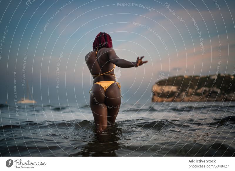 Schwarze Frau im Bikini geht im Meer spazieren Spaziergang MEER Strand Urlaub sorgenfrei Tourist Natur Sonnenuntergang Feiertag genießen Badebekleidung Wasser