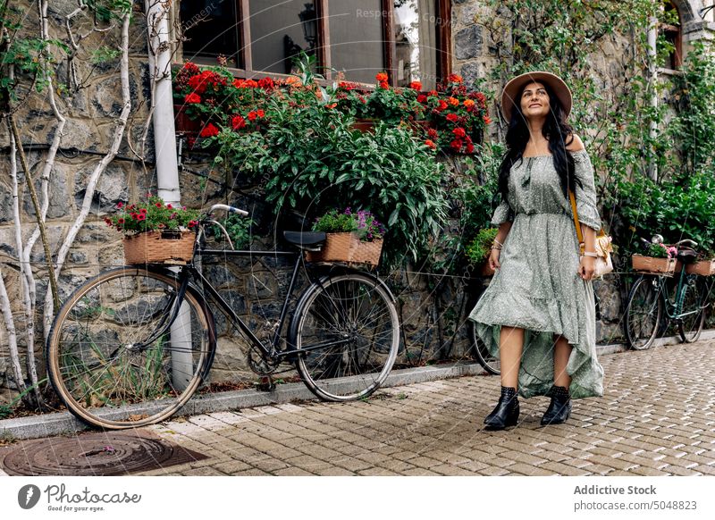 Glückliche Touristin auf der Straße Frau romantisch Spaziergang Straßenbelag erkunden Lächeln Steinwand Fahrrad Gebäude Erwachsener heiter lässig Sonnenhut