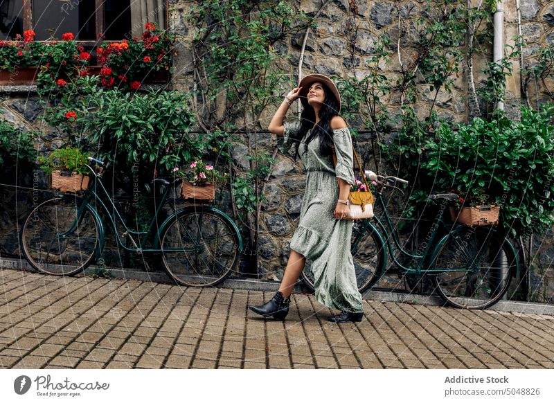 Glückliche Touristin auf der Straße Frau romantisch Spaziergang Straßenbelag erkunden Lächeln Steinwand Fahrrad Gebäude Erwachsener heiter lässig Sonnenhut