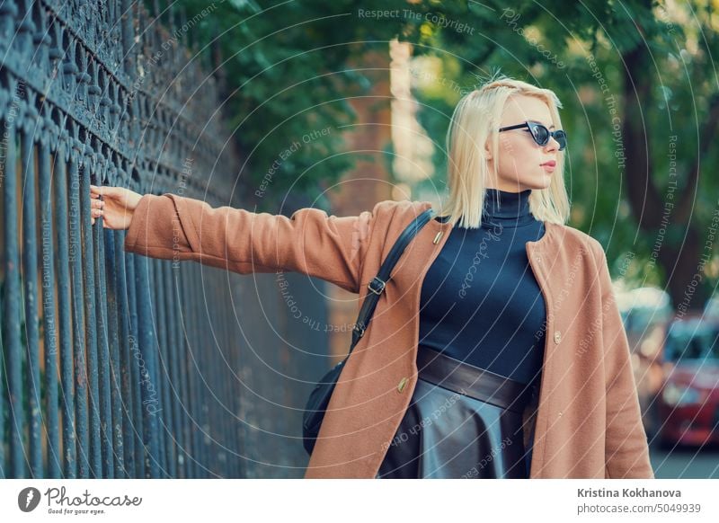 Mysteriöse stilvolle blonde Mädchen geht durch die europäische Metropole, hält den alten Zaun. Porträt der jungen Frau im Herbst schick aussehen. Reisen Konzept
