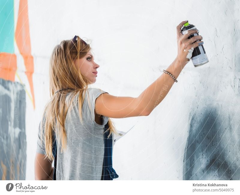 Schöne junge blonde Mädchen machen Graffiti von großen Auge mit Aerosol Spray auf städtischen Straßenwand. Kreative Kunst. Talentierte Studentin in Jeans-Overall Zeichnung Bild