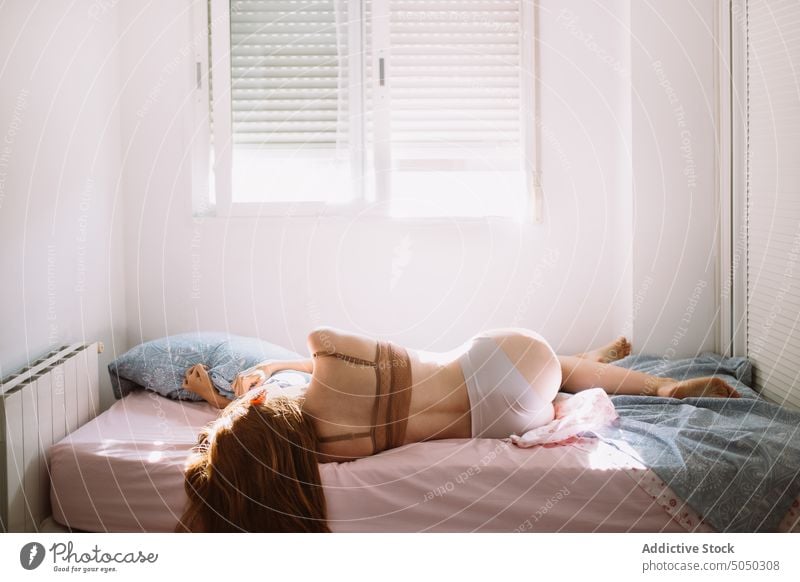 Schlanke Frau im BH auf dem Bett liegend am Fenster Morgen Dehnung wach aufwachen Sonnenlicht früh sinnlich Dessous LAZY Kopfkissen Schlafzimmer ruhen