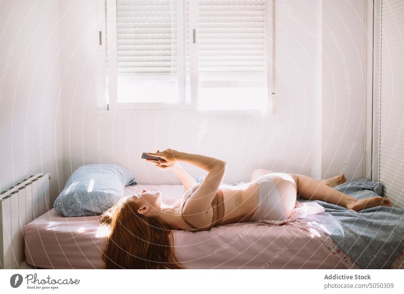 Schlanke Frau in Dessous auf dem Bett liegend mit Smartphone sinnlich benutzend Browsen Schlafzimmer Apparatur Morgen Internet Gerät schlank heimwärts