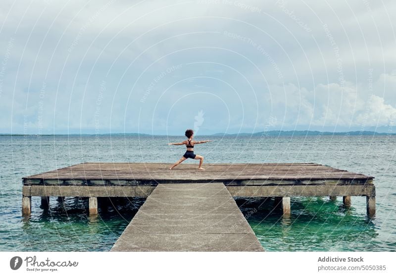 Frau macht Yoga auf schäbigem Pier im Meer meditieren Zen Asana virabhadrasana Krieger-Pose Gleichgewicht friedlich Wellness MEER Kai ruhig Erholung Achtsamkeit