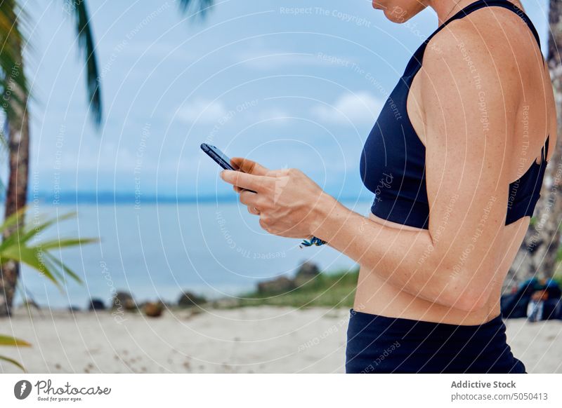 Anonyme Frau prüft Smartphone am tropischen Strand erstaunt Urlaub benutzend Sommer aufgeregt Lachen Meeresufer Feiertag Nachricht Apparatur ethnisch hispanisch