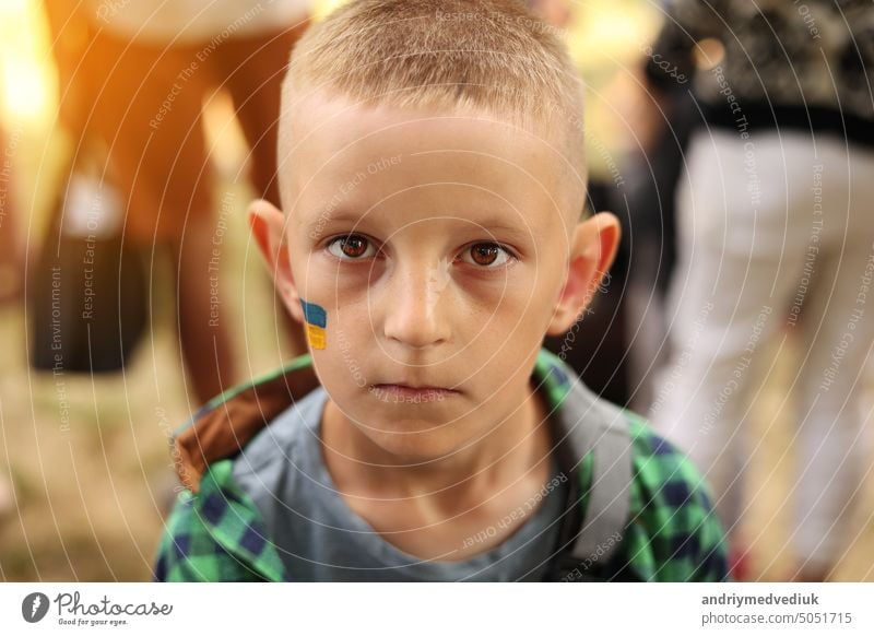 Nahaufnahme eines lächelnden Kindes mit aufgemalter ukrainischer Flagge im Gesicht. Protest gegen den russischen Krieg Invasion in der Ukraine. Ukrainische Flagge, Demonstranten Konzept