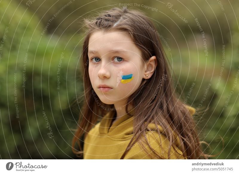das Gesicht eines verängstigten Mädchens, auf die Wange gemalt in den gelb-blauen Farben der ukrainischen Flagge, eine Bitte um Hilfe. Kinder bitten um Frieden. Hochwertiges Foto. Foto in hoher Qualität