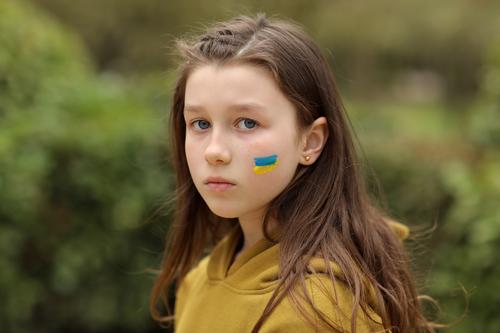 das Gesicht eines verängstigten Mädchens, auf die Wange gemalt in den gelb-blauen Farben der ukrainischen Flagge, eine Bitte um Hilfe. Kinder bitten um Frieden. Hochwertiges Foto. Foto in hoher Qualität