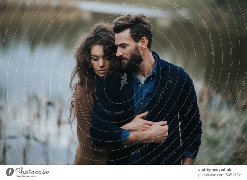 Zwei kaukasische Liebende in der Nähe des Sees. Junges Paar umarmt sich an einem Herbsttag im Freien. Ein bärtiger Mann und eine lockige Frau in der Liebe. Valentinstag. Konzept der Liebe und Familie