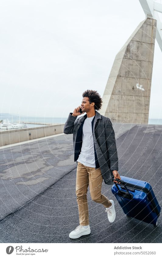 Schwarzer Tourist spricht in der Stadt mit Smartphone Mann Koffer reden Spaziergang Urlaub Großstadt Ausflug benutzend Telefonanruf Reisender sprechen männlich
