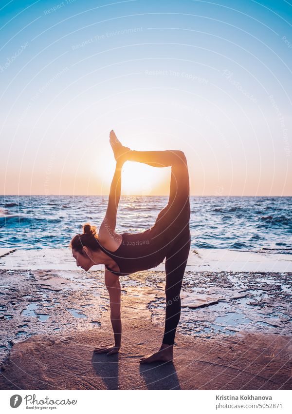 Schlanke Frau in schwarzem Bodysuit übt Yoga in der Nähe von Meer oder Ozean bei Sonnenaufgang Licht. Flexibilität, Stretching, Fitness, gesunder Lebensstil.