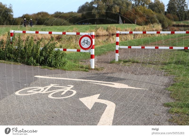 links oder rechts , aber nicht geradeaus - Fahrradweg mit richtungsweisenden Markierungen und Verbotsschild am rot-weißen Zaun Radweg Schild Verkehrsschild