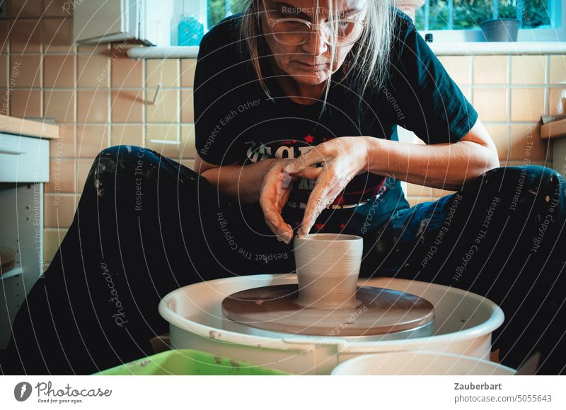 Töpfern, Frau in ihrer Töpferwerkstatt formt konzentriert ein Gefäß aus Ton auf der Töpferscheibe Wände hochziehen pulling walls Hände Handwerk Hobby Kunst