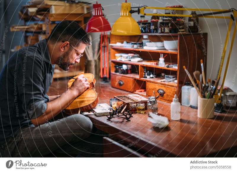 Geigenbauer beim Lackieren einer Geige in der Werkstatt Kunsthandwerker Firnis Zupfinstrumentenmacher polnisch Kunstgewerbler Meister professionell hölzern