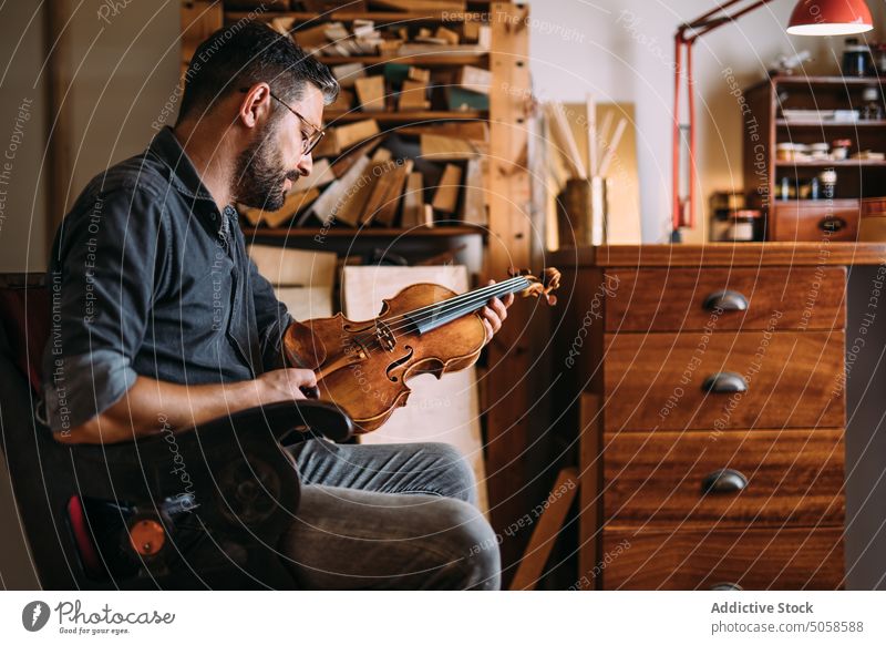 Männlicher Geigenbauer mit Geige in der Werkstatt Mann Instrument Zupfinstrumentenmacher Basteln Atelier professionell klassisch Arbeitsplatz Kunsthandwerker