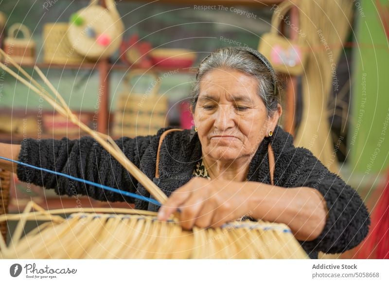 Ältere hispanische Frau beim Basteln eines Graskorbs Handwerkerin Weben Korb Fokus trocknen handgefertigt Tisch Rentnerin Weide Korbwaren älter Senior gealtert