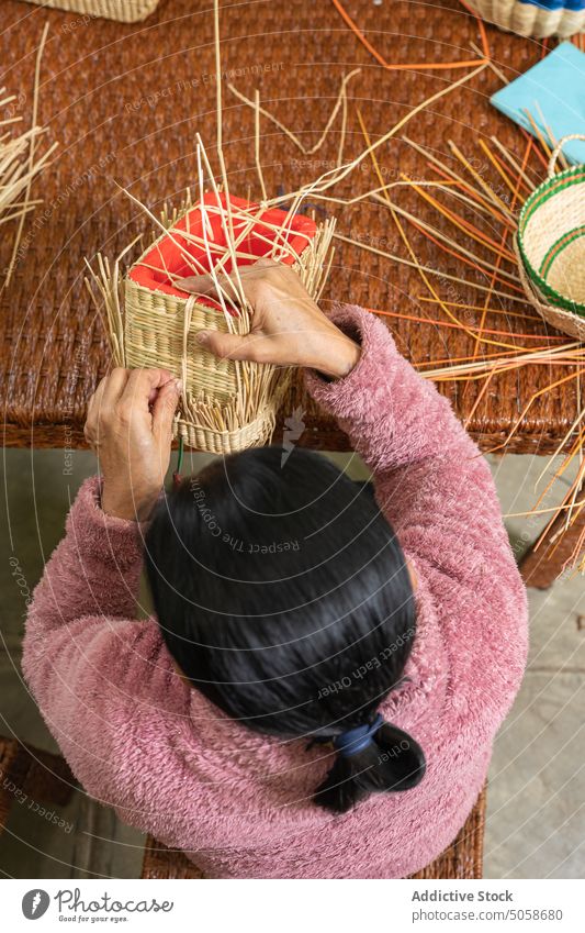 Anonyme Kunsthandwerkerin bei der Herstellung eines Strohkorbs Handwerkerin Weben Korb Tisch Werkstatt handgefertigt trocknen Fähigkeit Frau Korbwaren reif