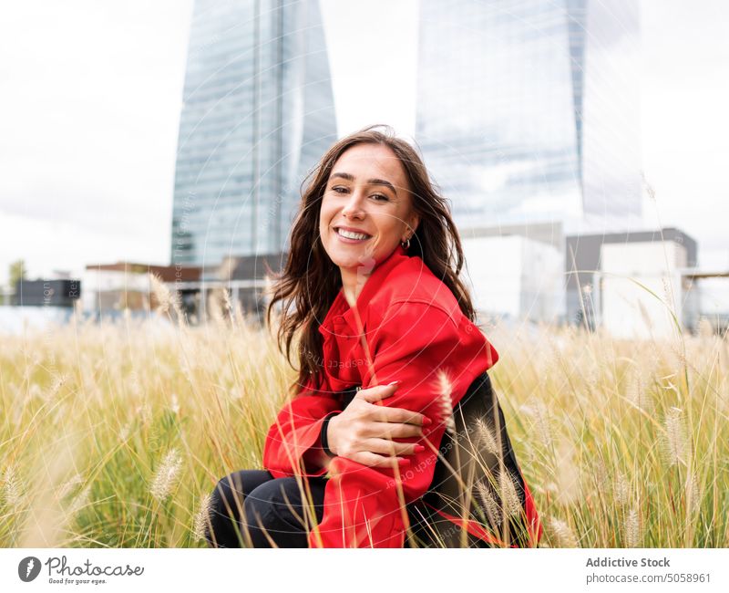 Stilvolle glückliche Frau sitzt im Gras im Park urban Großstadt Voute Sommer Wochenende jung Rasen brünett tagsüber Lifestyle Persönlichkeit Saison
