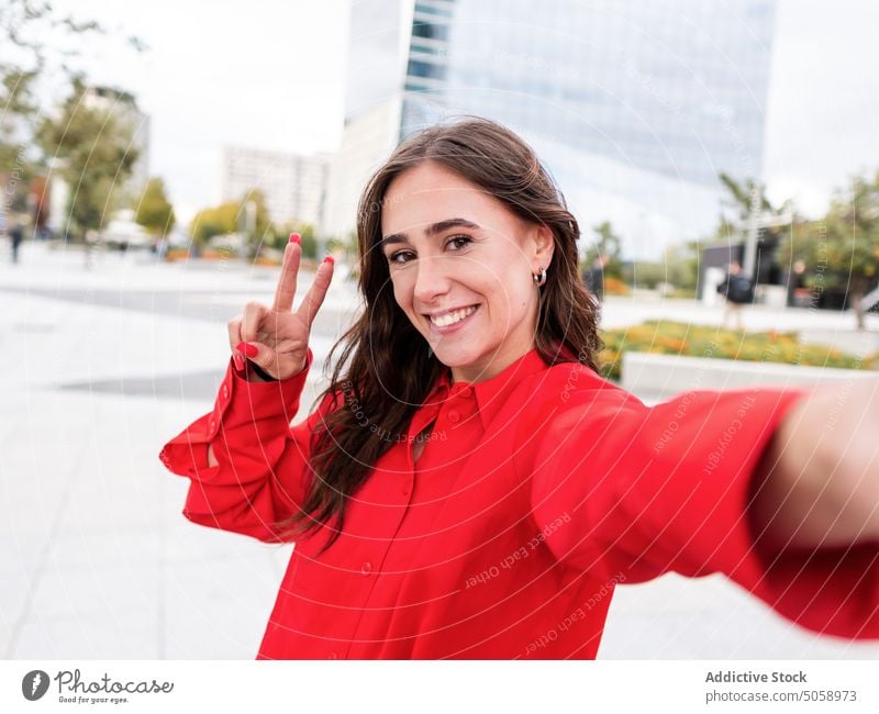 Glücklich stilvolle weibliche Aufnahme selfie auf der Straße Frau Selfie Lächeln v-Zeichen gestikulieren urban Stil braune Haare jung lange Haare Funktelefon