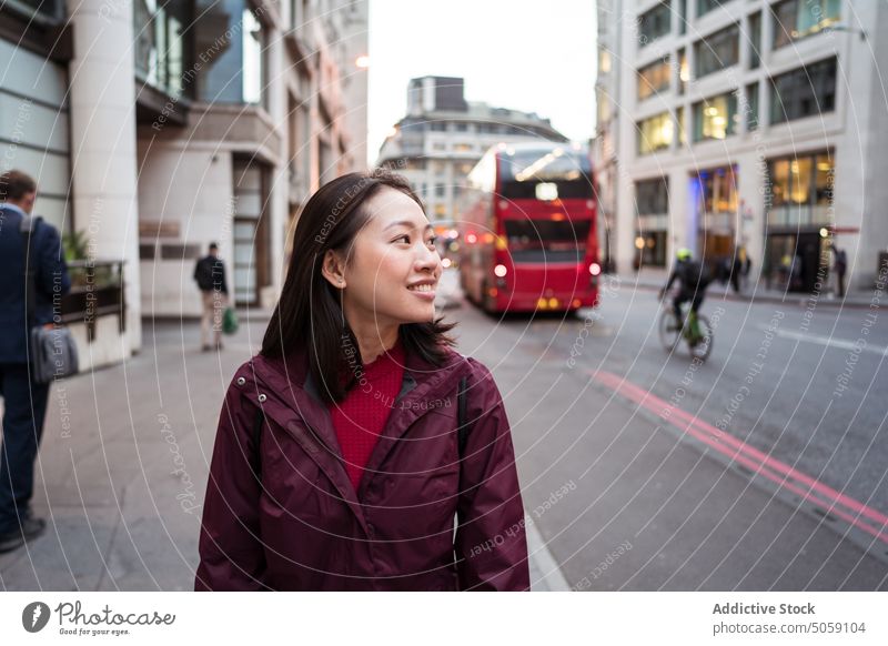 Fröhliche asiatische Frau auf der Straße Spaziergang Lächeln Bürgersteig Tourist Glück Oberbekleidung bewundern Abend London England vereinigtes königreich