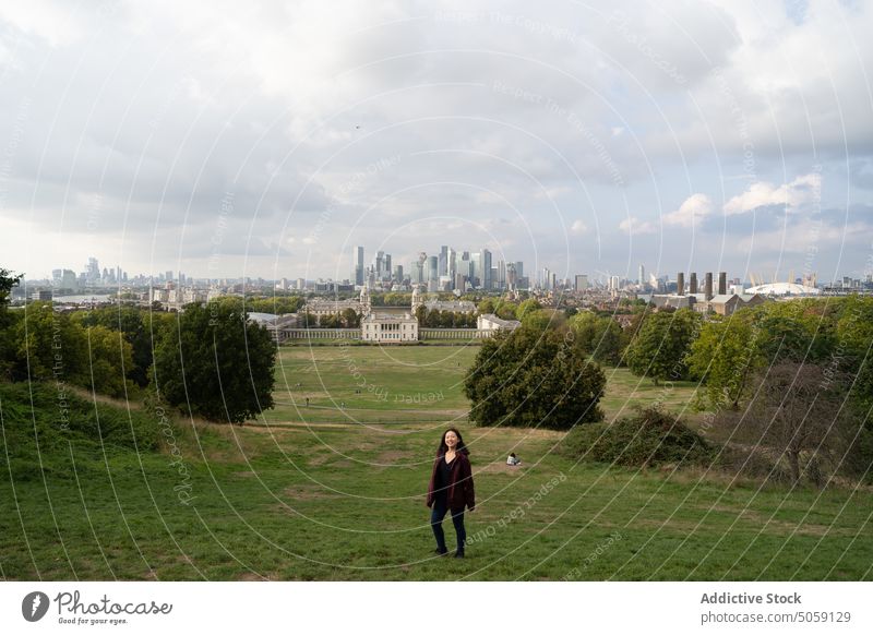Weiblicher Reisender auf einem Feld in der Nähe der Stadt Frau Großstadt Gras Gebäude wolkig Himmel Sommer Baum London Greenwich England vereinigtes königreich